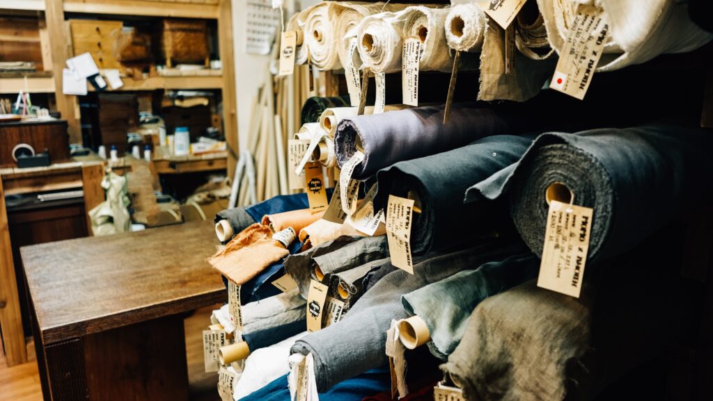 Rolls of fabric on a shelf, highlighting material selection as part of the online bespoke tailoring process.