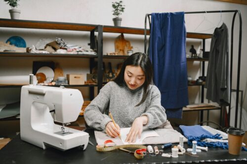 A woman seated at a table with sewing equipment, carefully crafting fabric pieces, symbolizing the art of bespoke tailoring