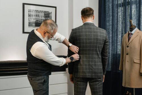 A tailor measuring a man's back with a tape measure, ensuring a perfect fit for a custom-made suit for men.